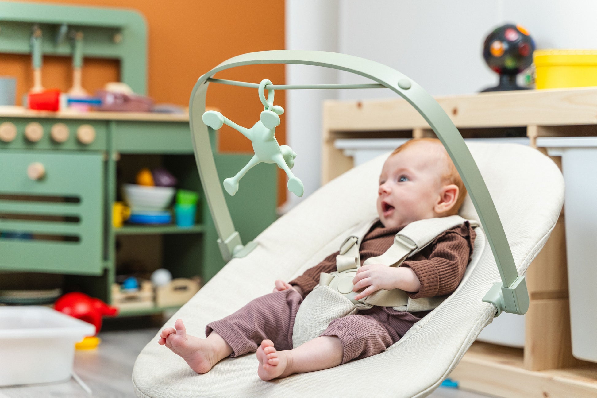 Glückliches Baby mit Silikonspielzeug in der Wippe